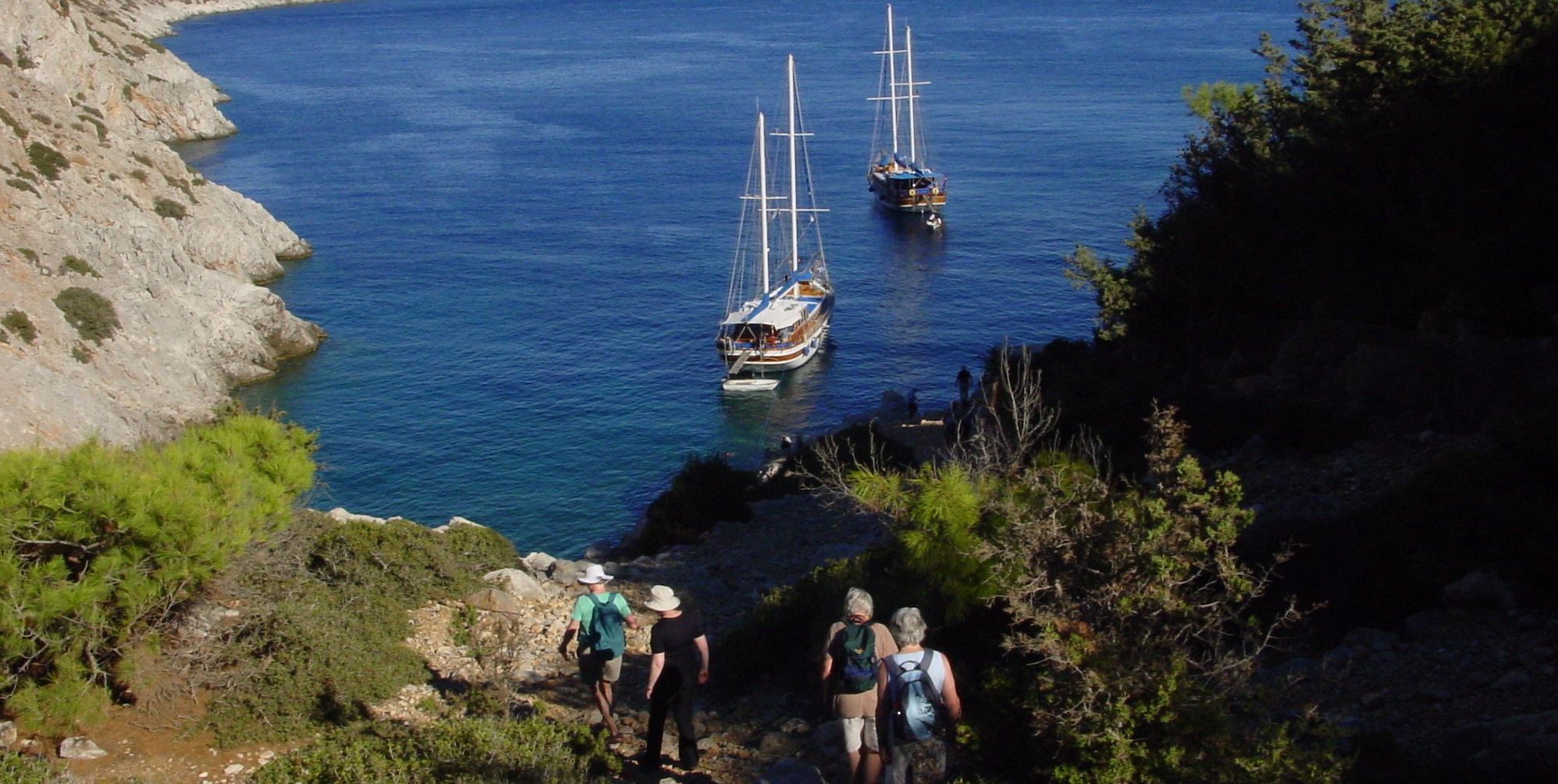 Four travelers hiking down to a cove where two gulets are anchored