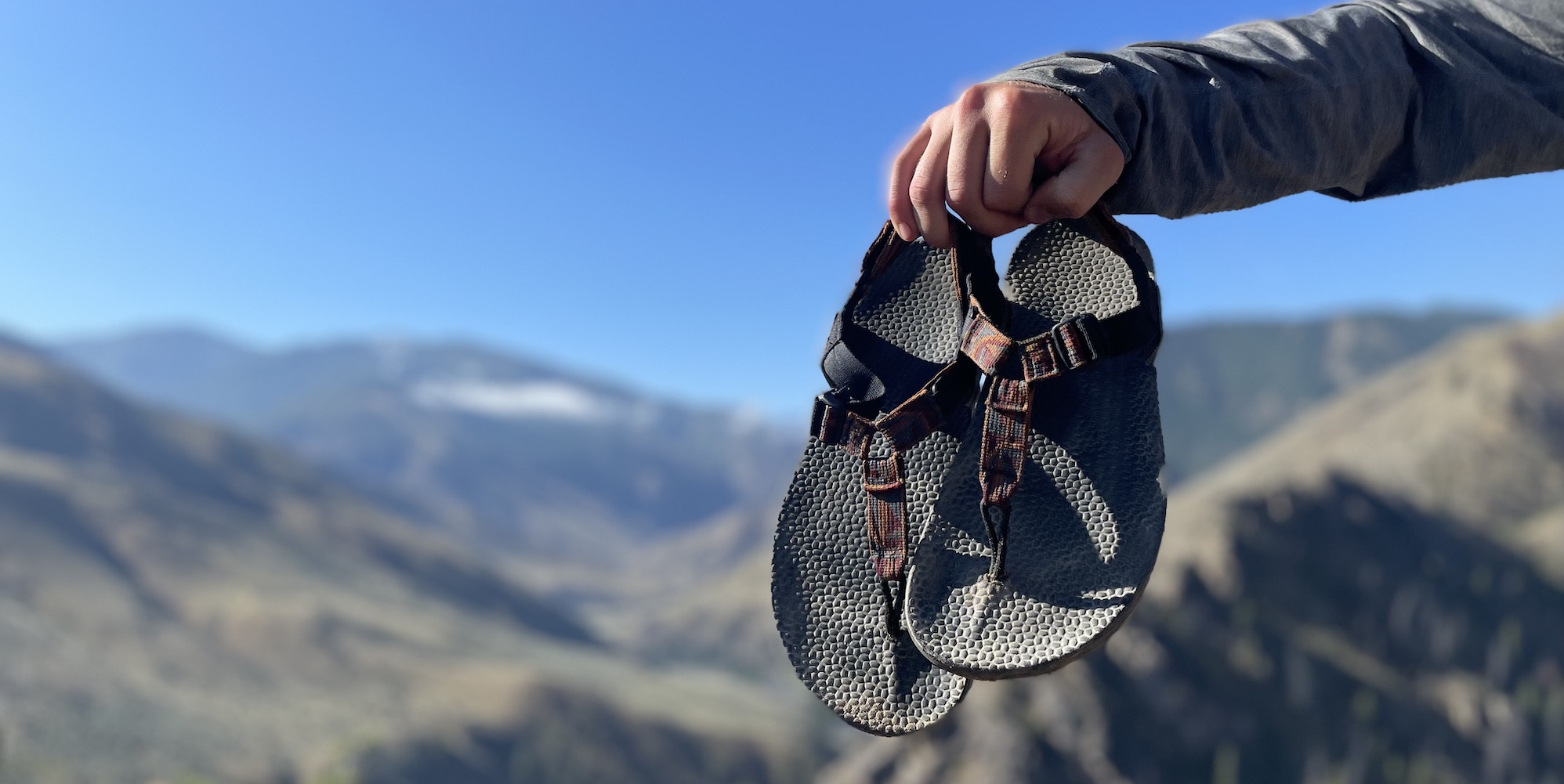 A person holding up a pair of bedrock sandals at the top of a hike in Idaho