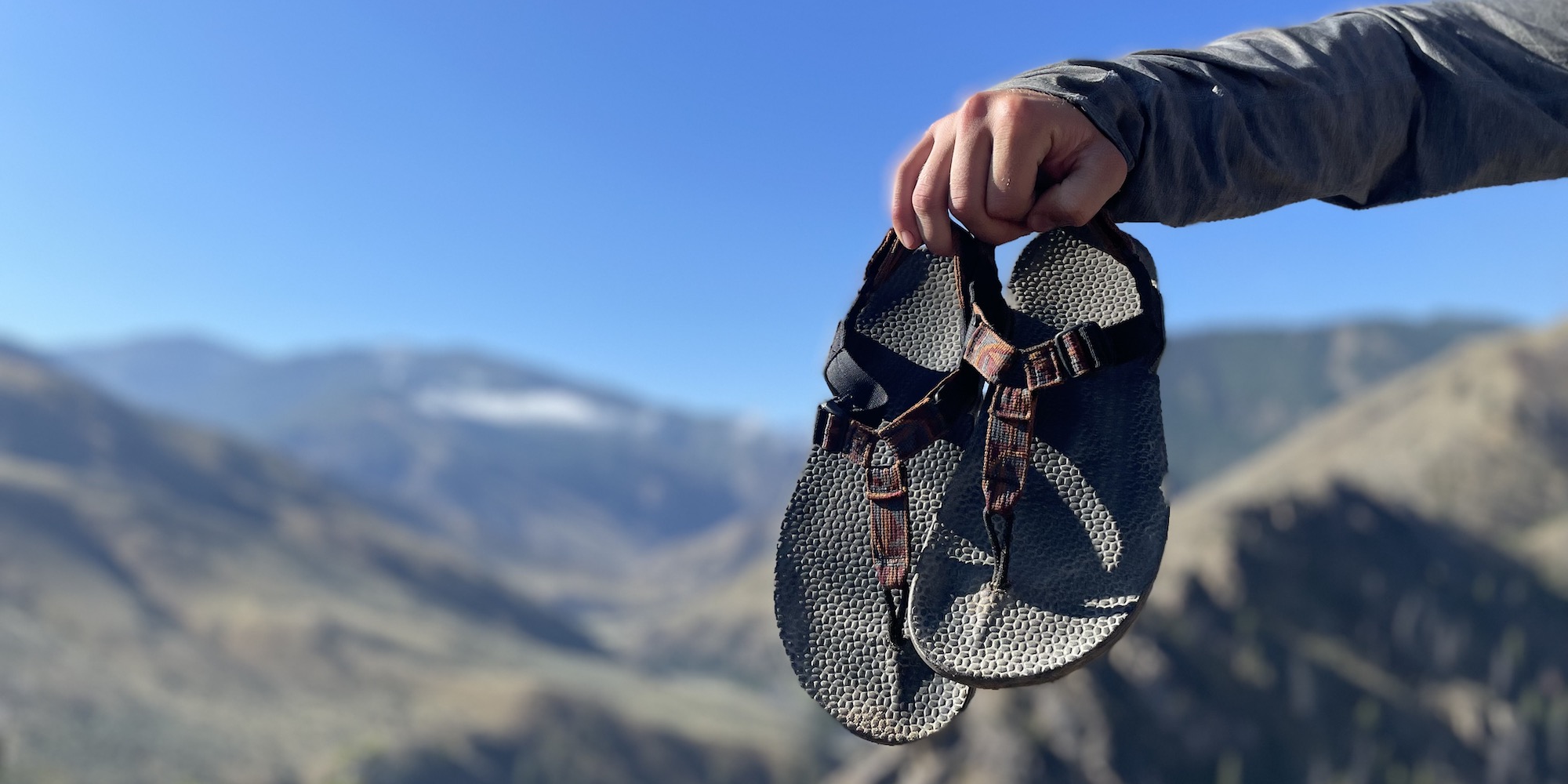 A person holding a pair of Bedrock sandals in Canyon Current color on a sunny day