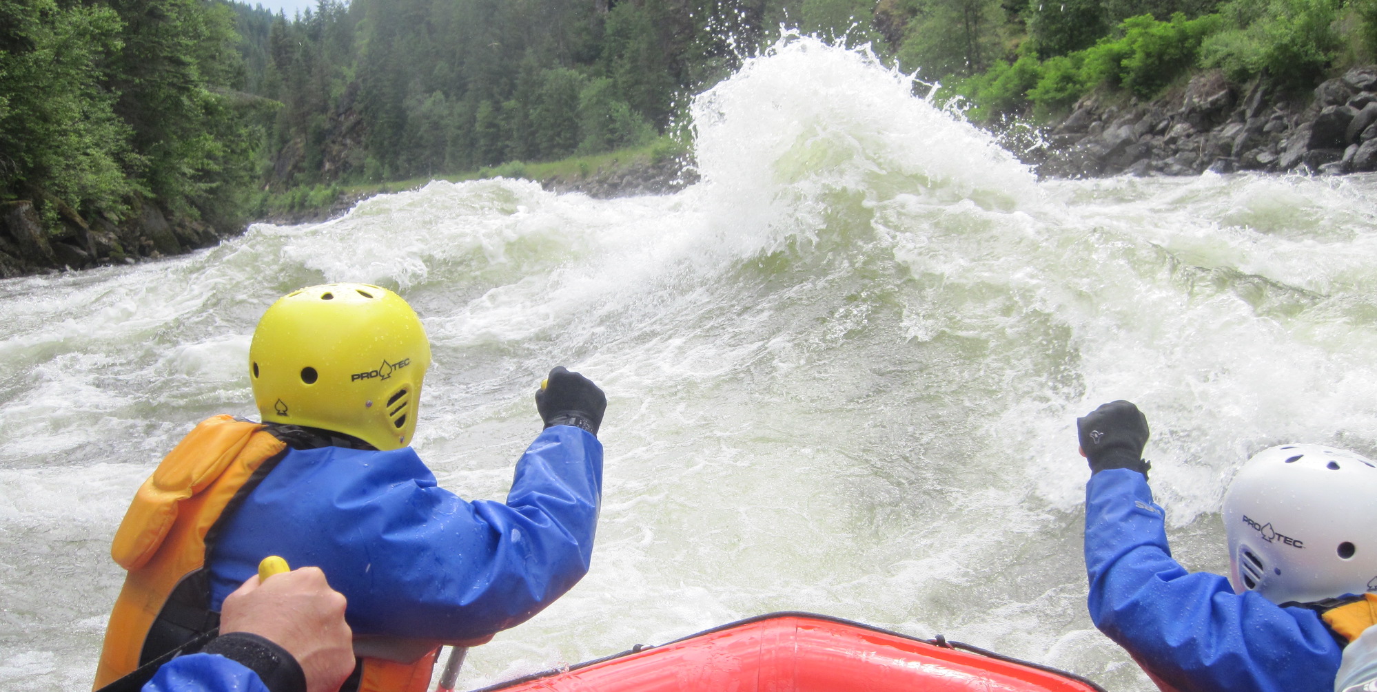 Two paddlers on a red boat looking directly at a huge whitewater wave in front of them on the Lochsa River