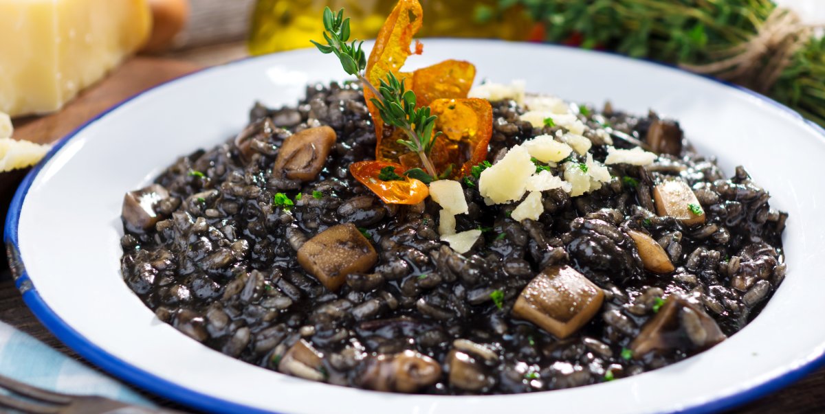 Squid ink black risotto in a white and blue plate topped with parmesan cheese and thyme 