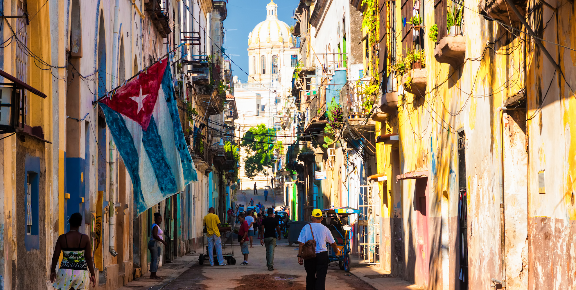 Small street view of colorful buildings and doorways while people walk the road down the middle in Cuba