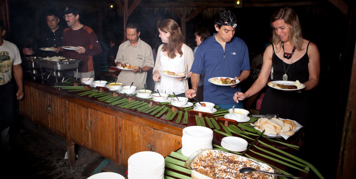 Group of guests serving themselves dinner around a green buffet table in the Galapagos
