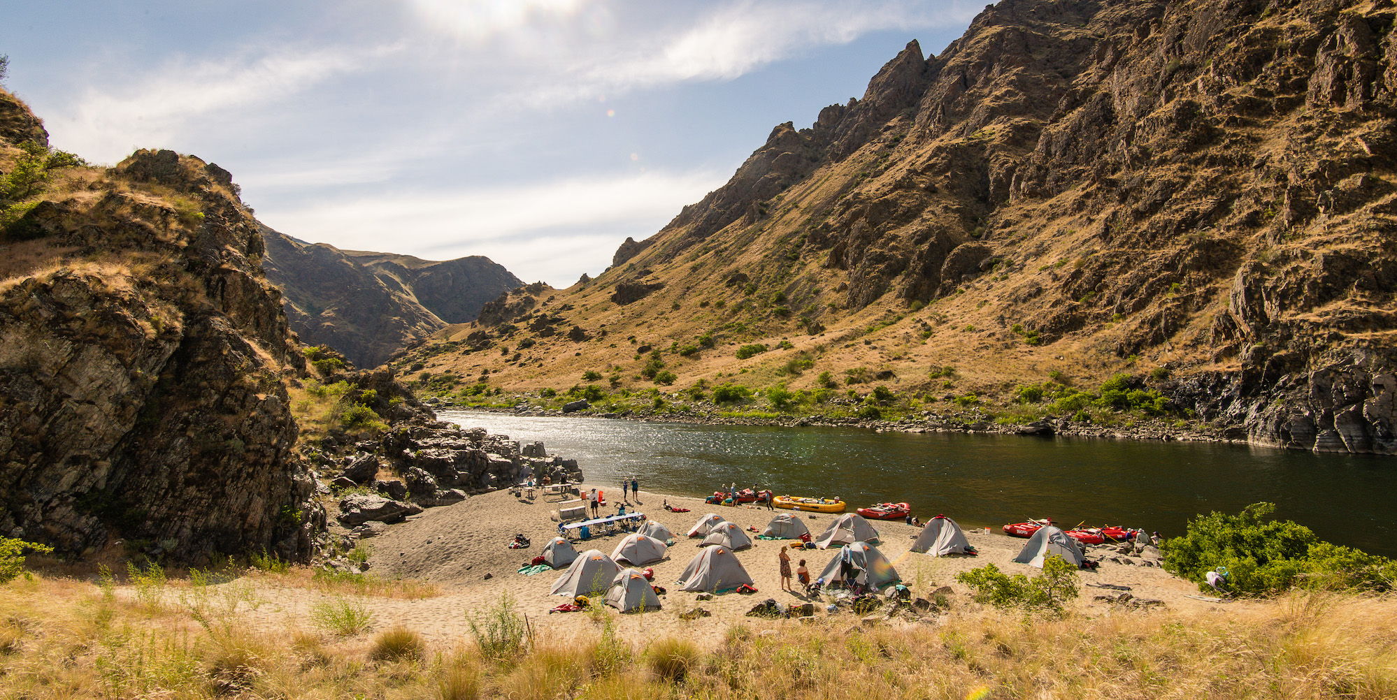 Tents sprawled on a wide sand beach along the Snake River through Hells Canyon
