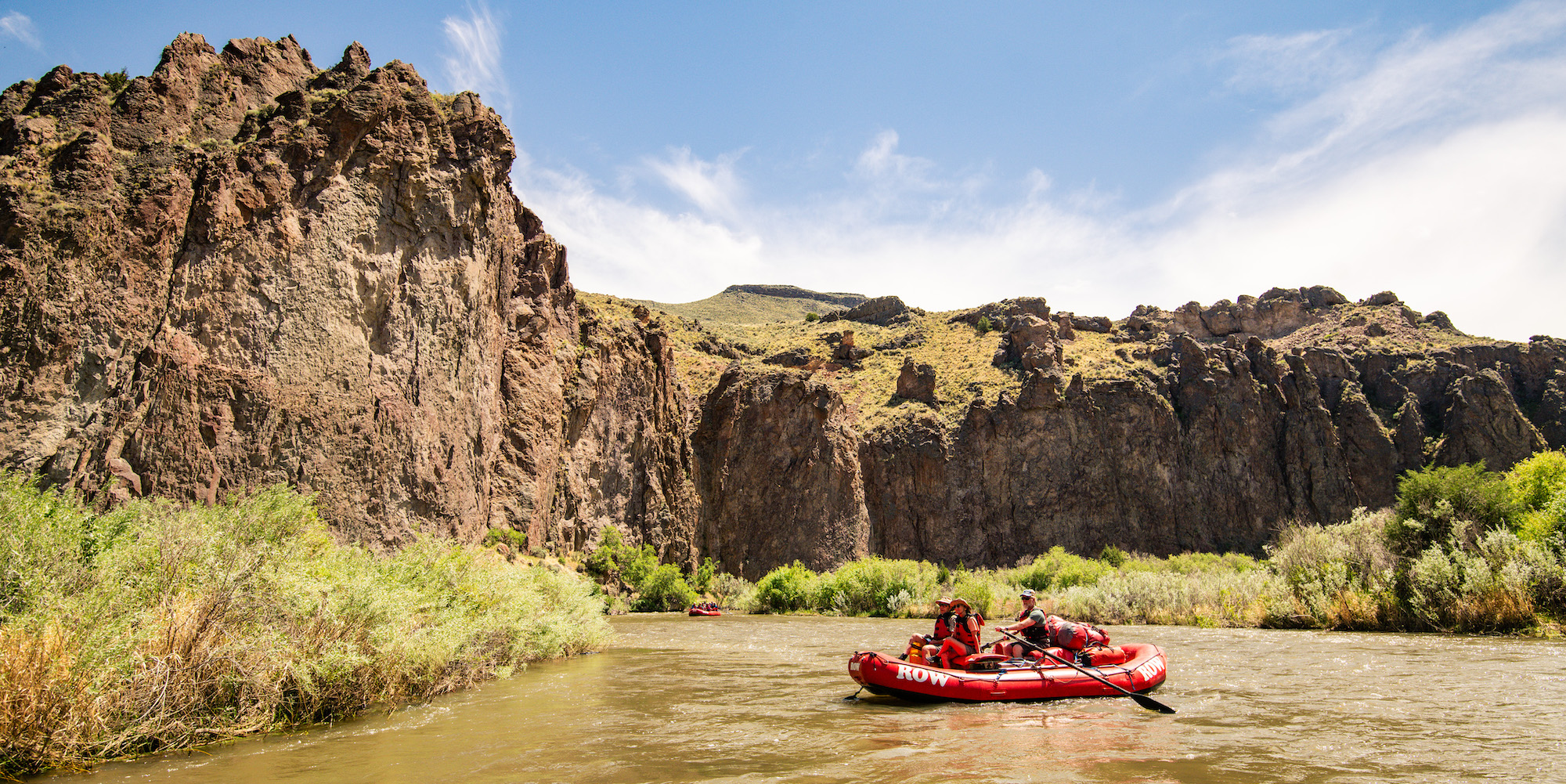 Two guests in a red ROW raft being rowed by a guide down the Bruneau River in Idaho
