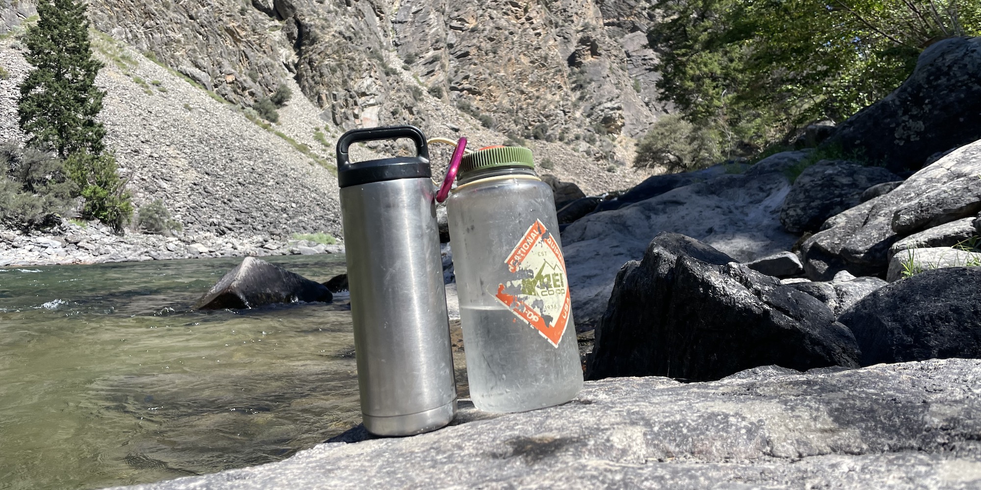 Insulated Yeti water bottle next to a Nalgene water bottle on a rock along the river
