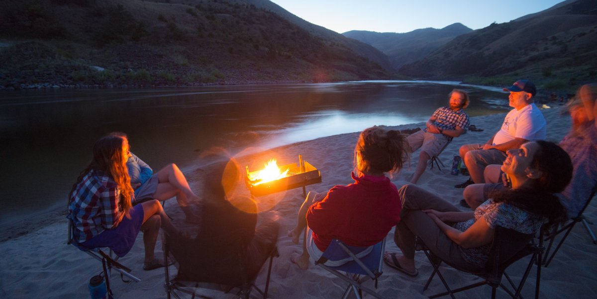 A group of campers around the fire using a fire pan to minimize their campfire impacts while on a river trip