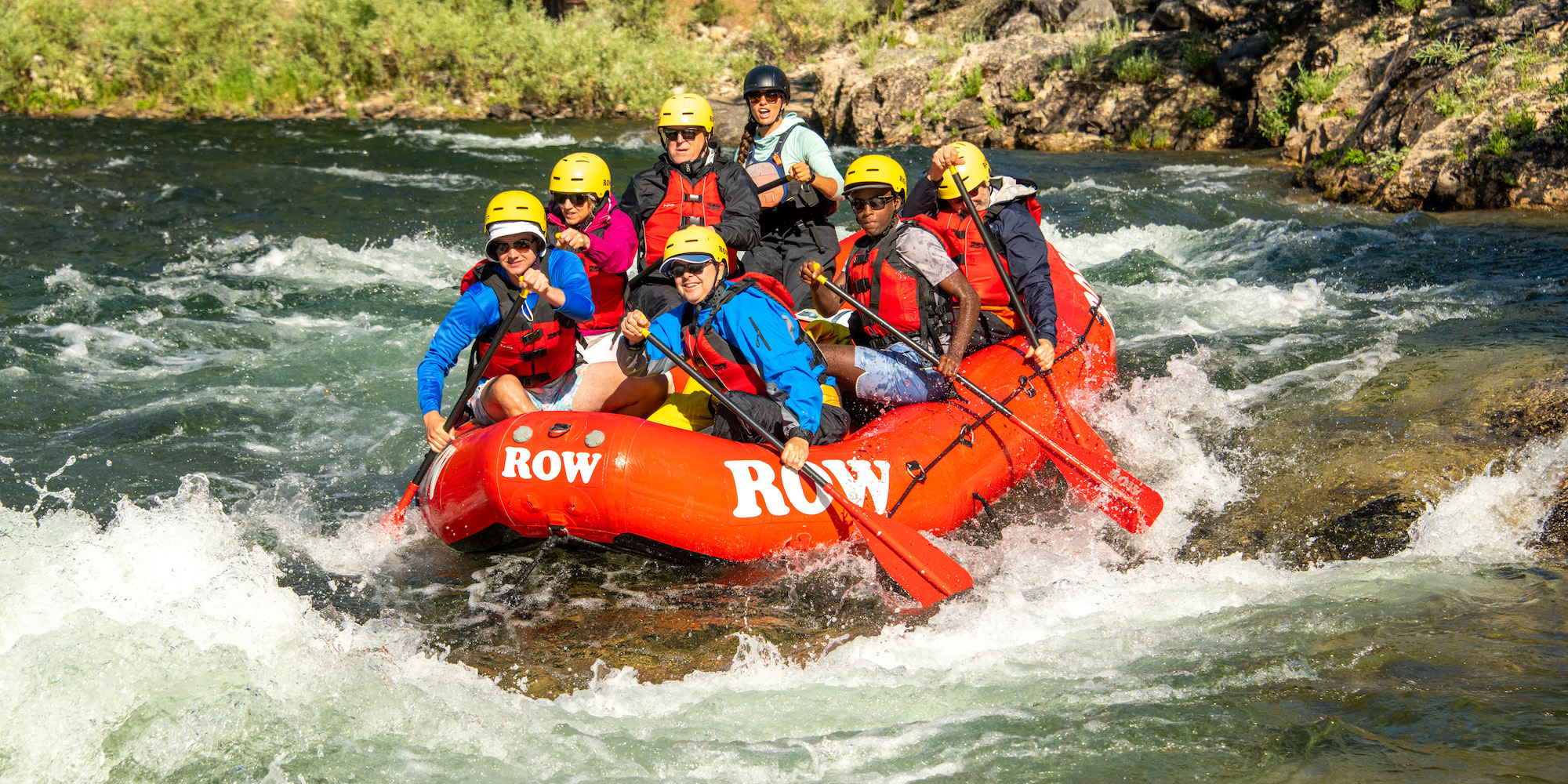 A group of people paddling town the Middle Fork Salmon River with a guide in a red raft on a sunny summer day