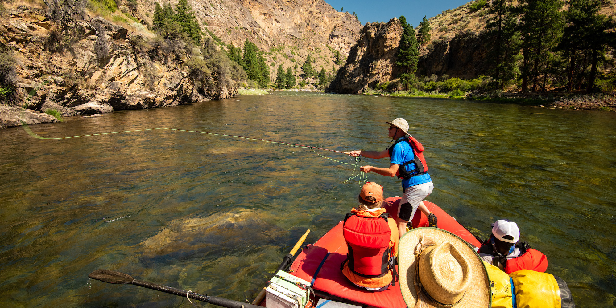 Person fishing off of a red oar raft on the Middle Fork Salmon River in the sun