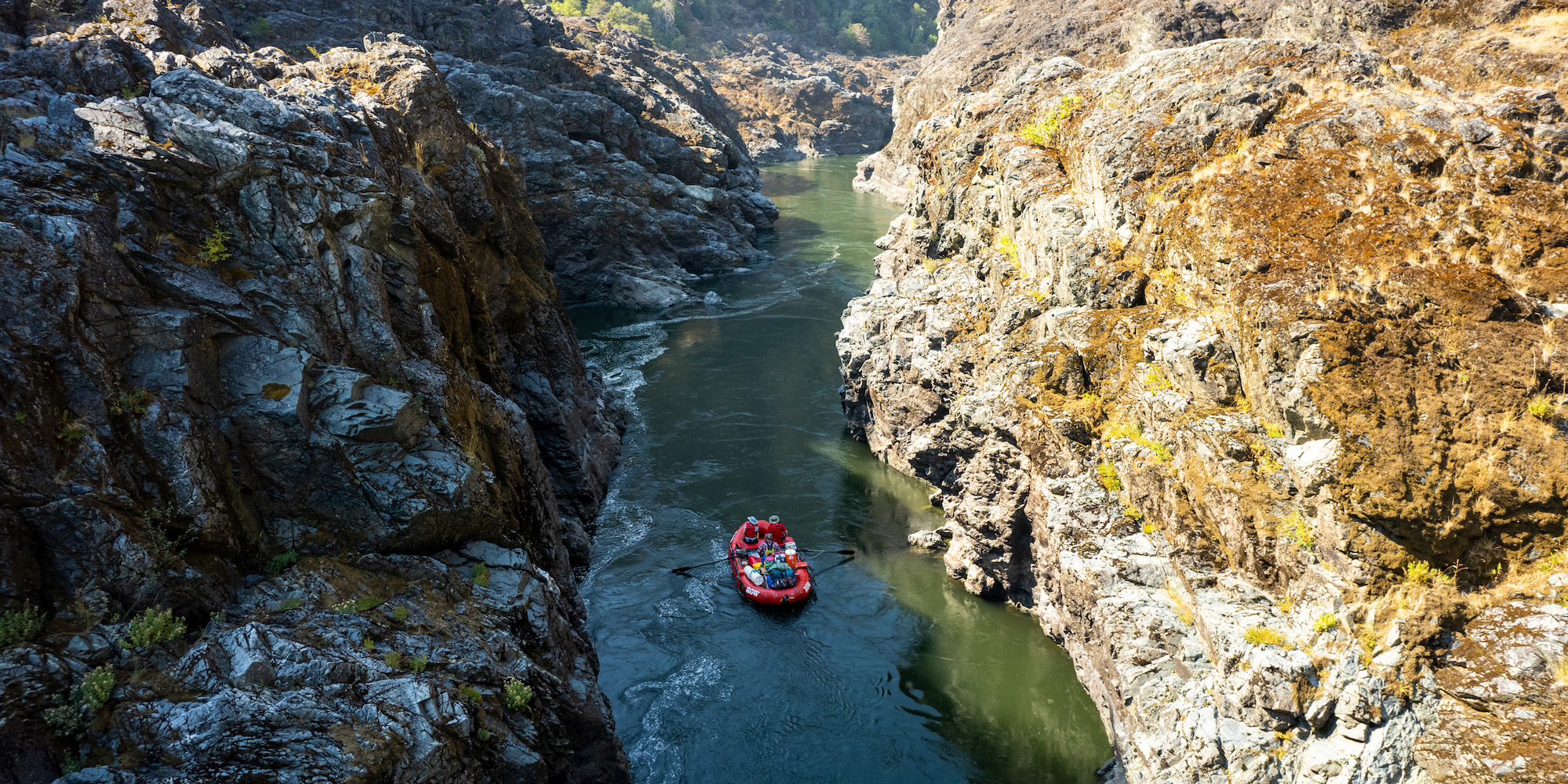 A red raft in between gorge walls moving downstream on the Rogue River