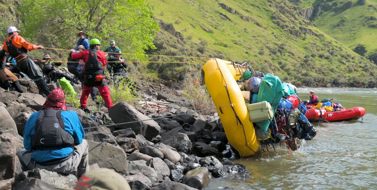 Group of raft guides flipping over a yellow raft full of gear on the river