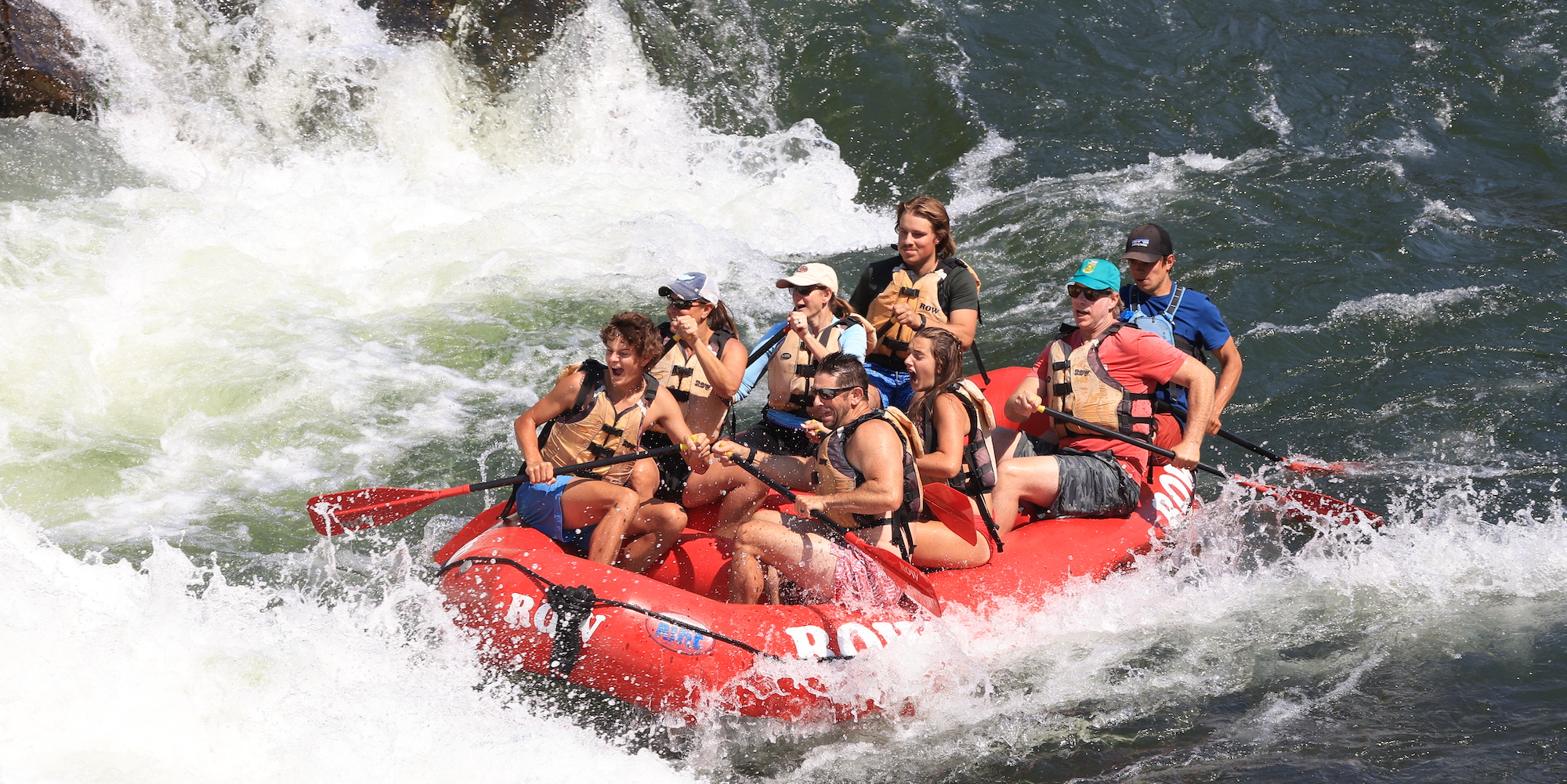 Group of people rafting the Clark Fork River in a red ROW Adventures raft on a hot summer day