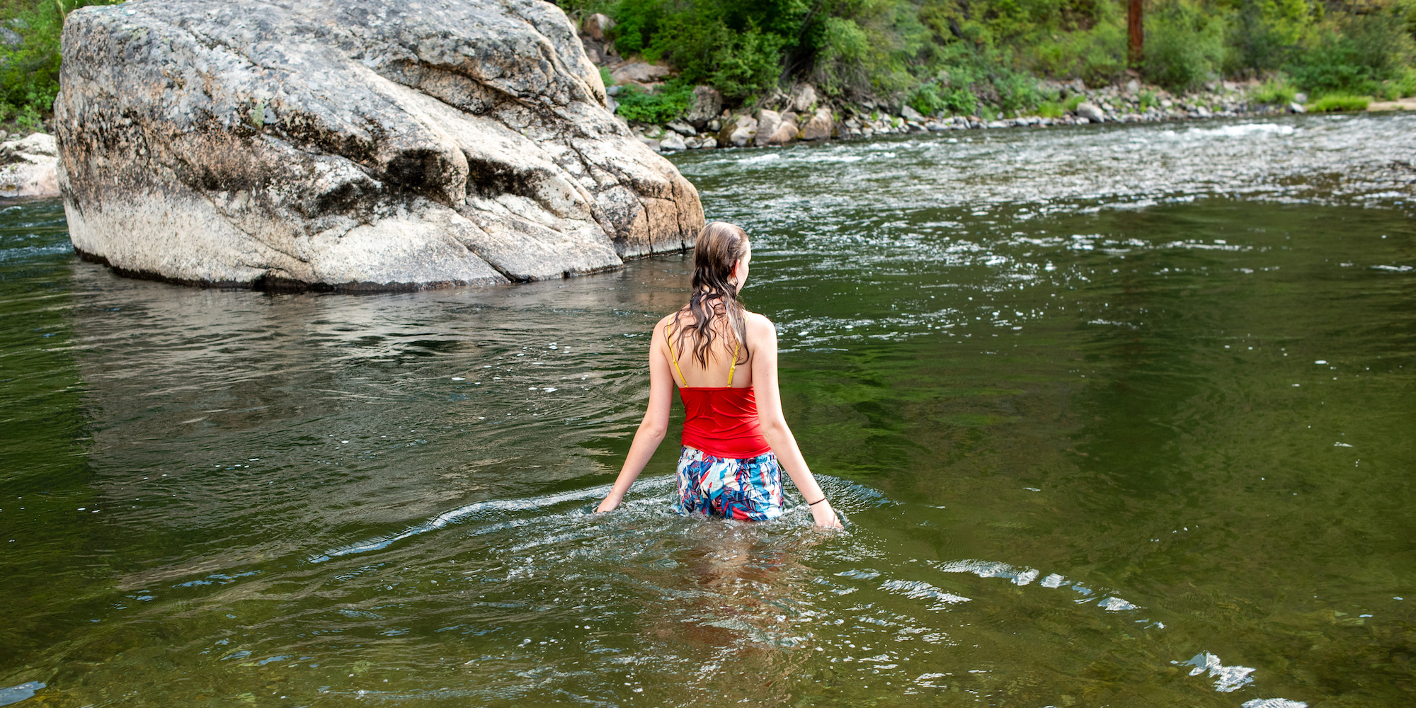 The back of a women getting ready to dive into the river by a boulder to cool off on a summer day