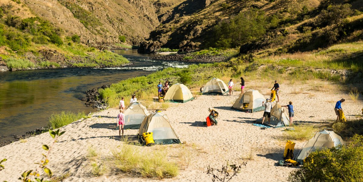 Guests taking down their tents on a sandy beach preparing for a day on the Snake River