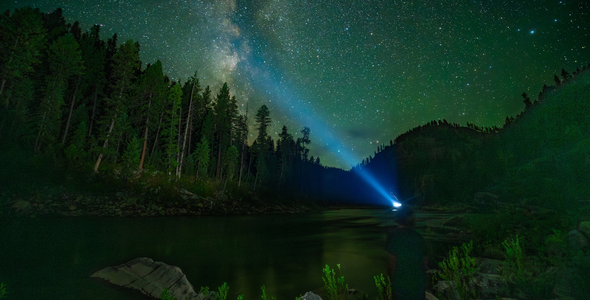 A person standing by the shores of the main salmon river at night with a headlamp on looking up at the mily way.