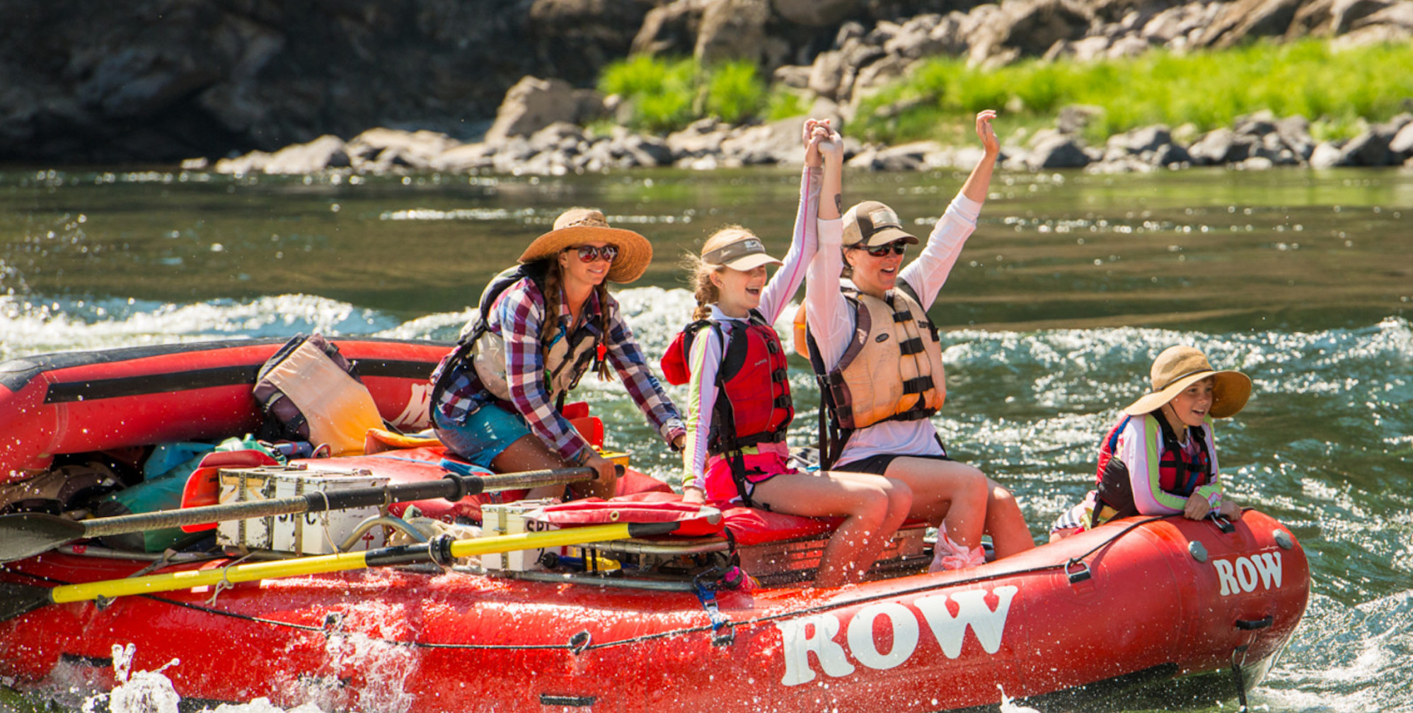 Mom on the front of a red raft with her daughter and son smiling and holding their arms up as they are rowed through a rapid on the Lower Salmon river