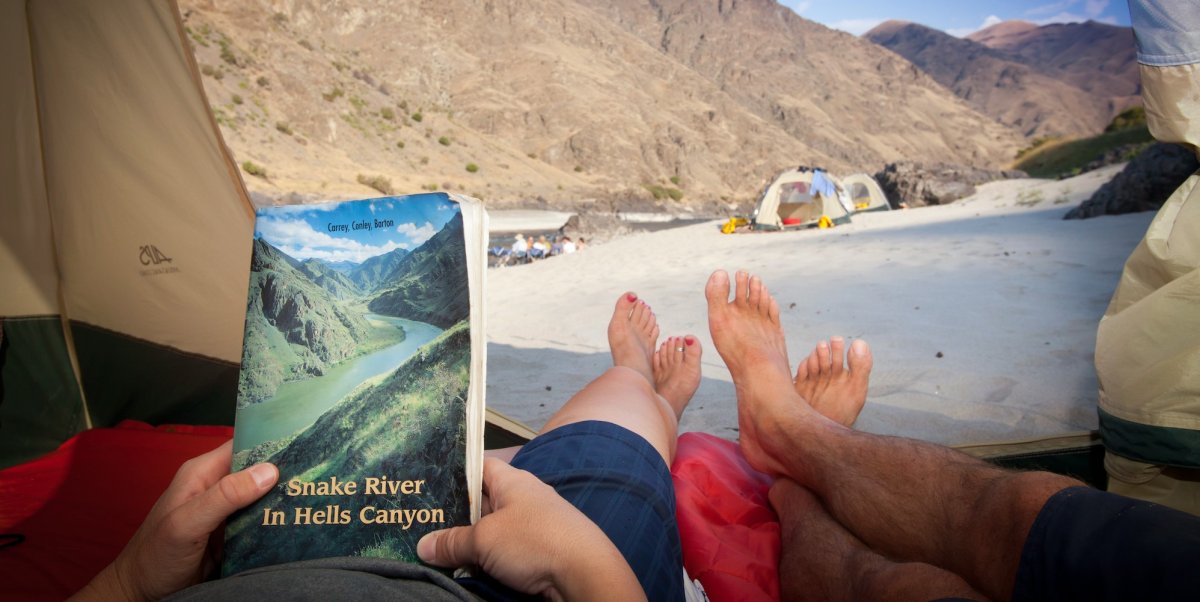Guests laying in a tent reading the Snake River guidebook overlooking the river