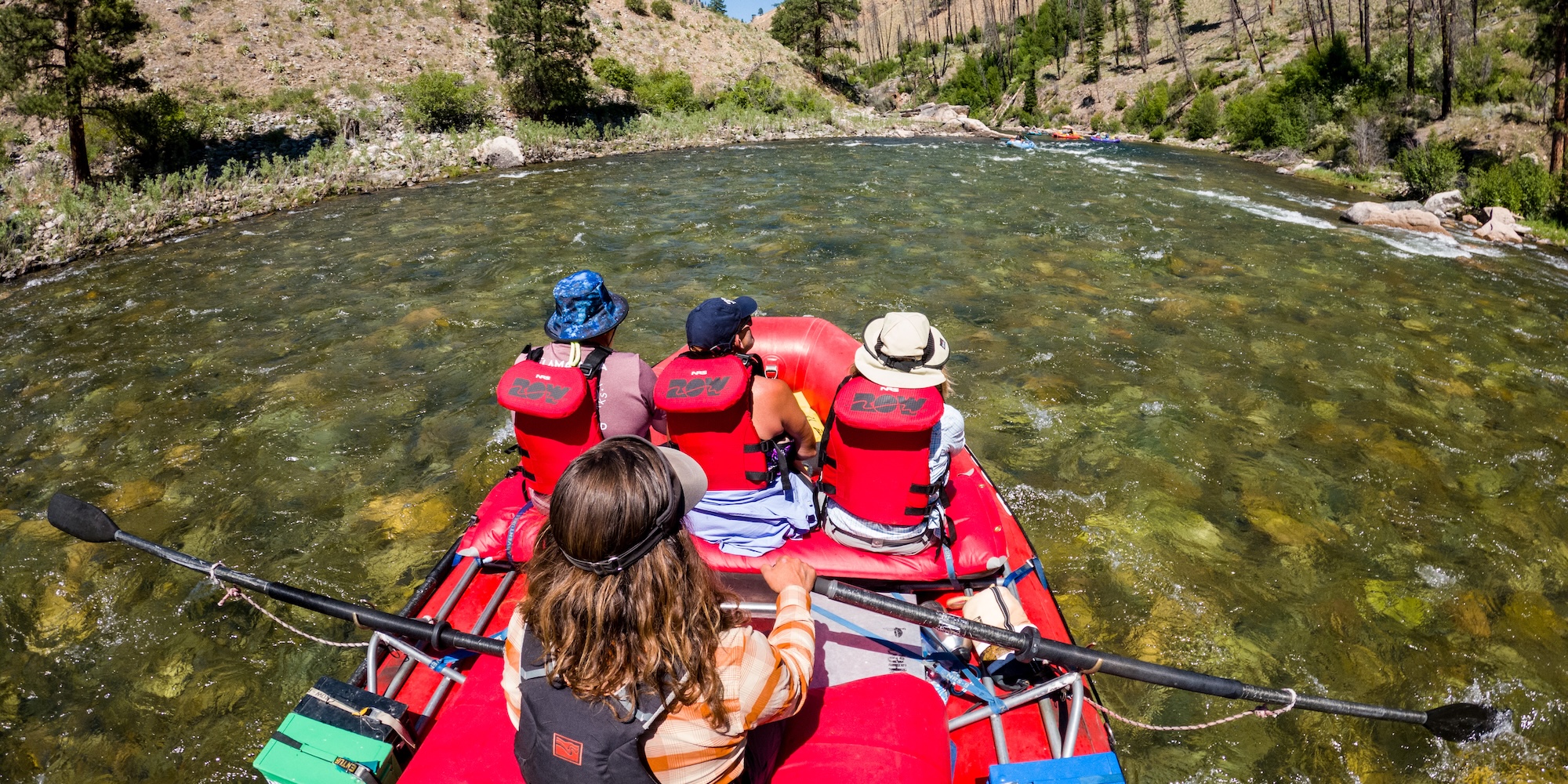 Raft crew floating through clear, shallow water on the Middle Fork of the Salmon River, moving slowly and intentionally through a quiet stretch of canyon.