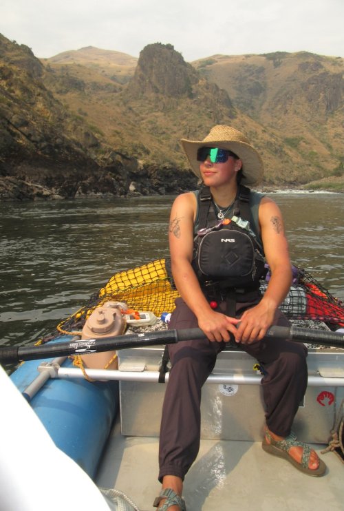 ROW Adventures river guide sitting in a raft rowing down a river with mountains and rapids behind them.