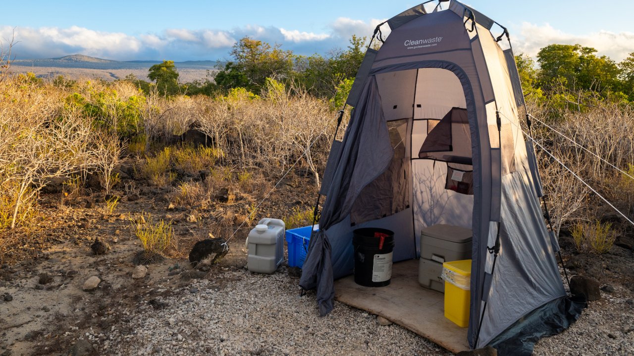 Inside the privacy bathroom tent showing buckets, a toilet, and bathroom supplies.