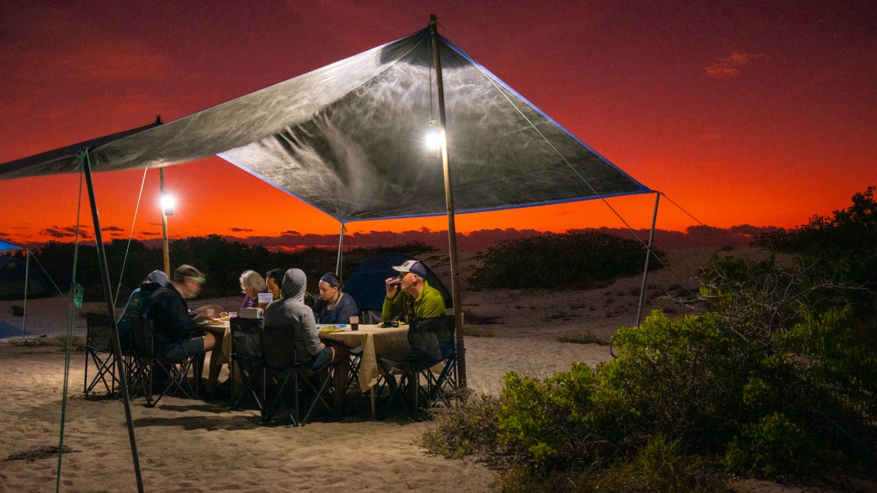 Tourists eating dinner on the beach beneath a red sunset