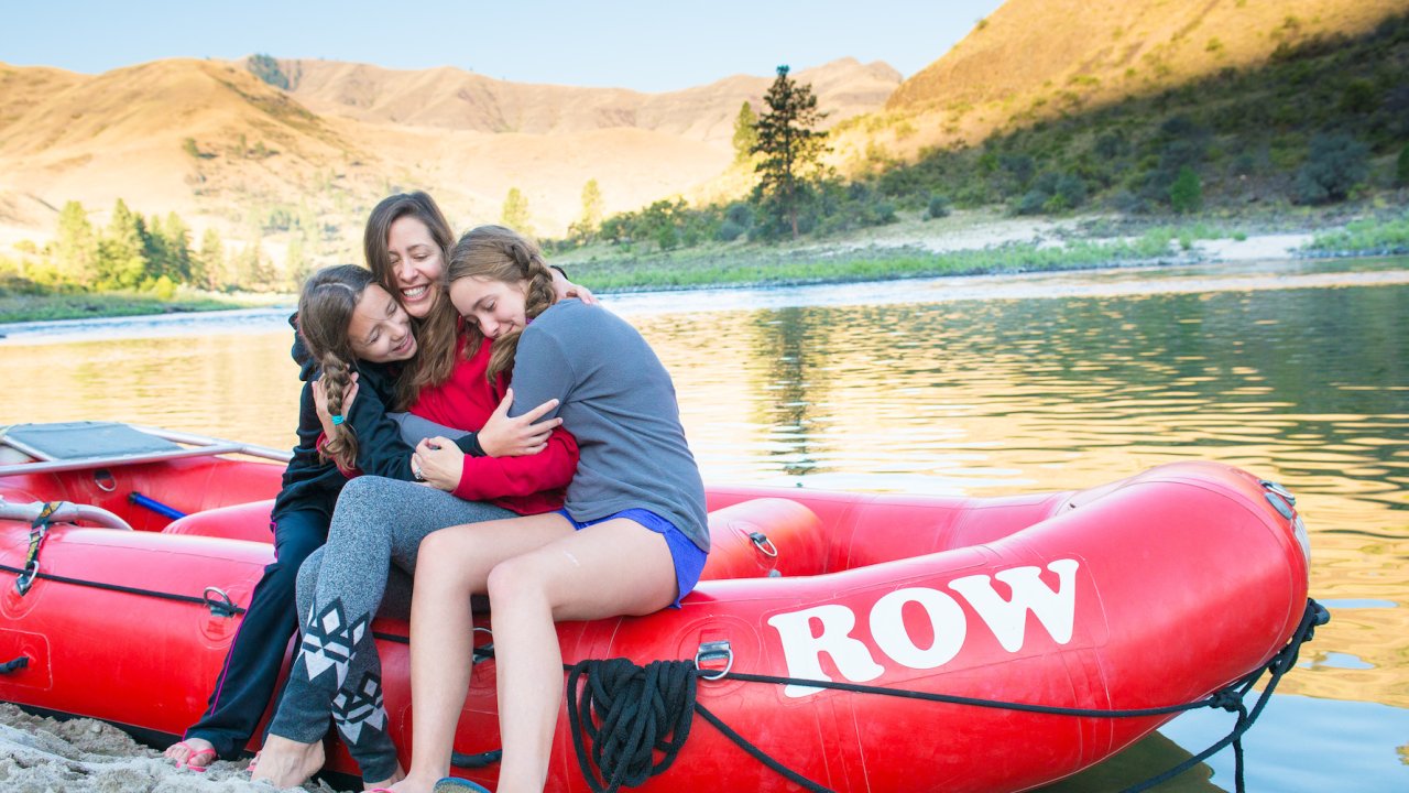 A mom with her two daughters sitting beside her on a red whitewater raft along the Salmon River