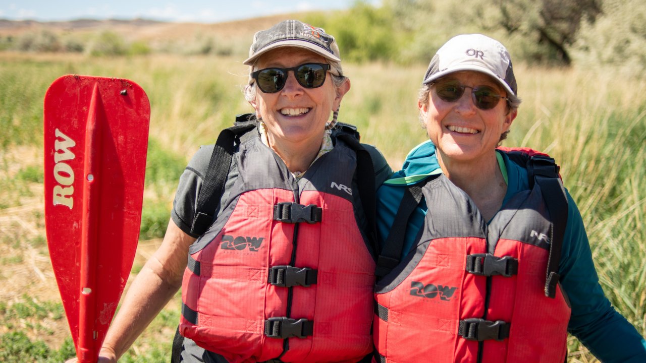 Two guests wearing red life jackets and the one on the left holding a red paddle smiling