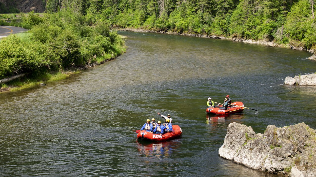 Two red rafts moving down flat water smiling up at the camera