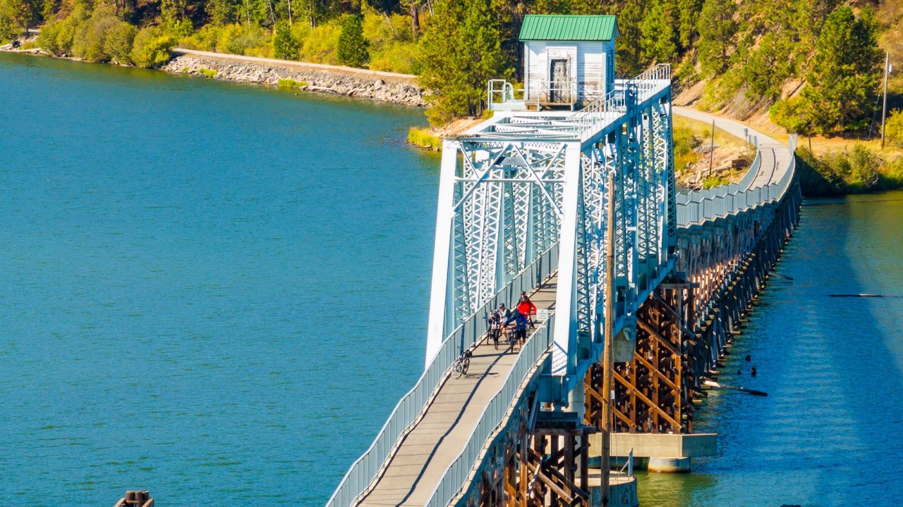 Group of cyclists crossing a steel bridge over a lake on a guided biking tour in Idaho