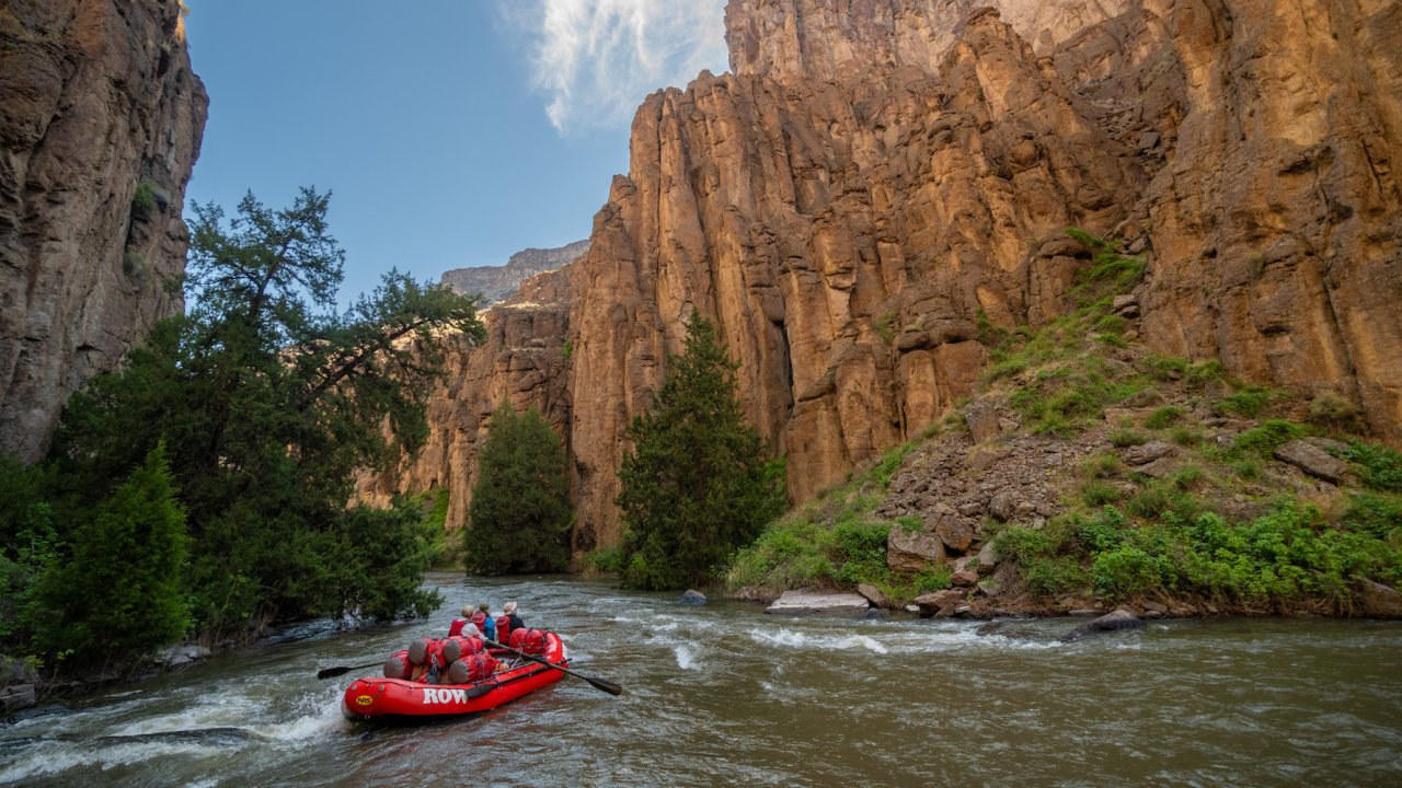 A red ROW raft floating down the Bruneau river with towering canyon walls on either side