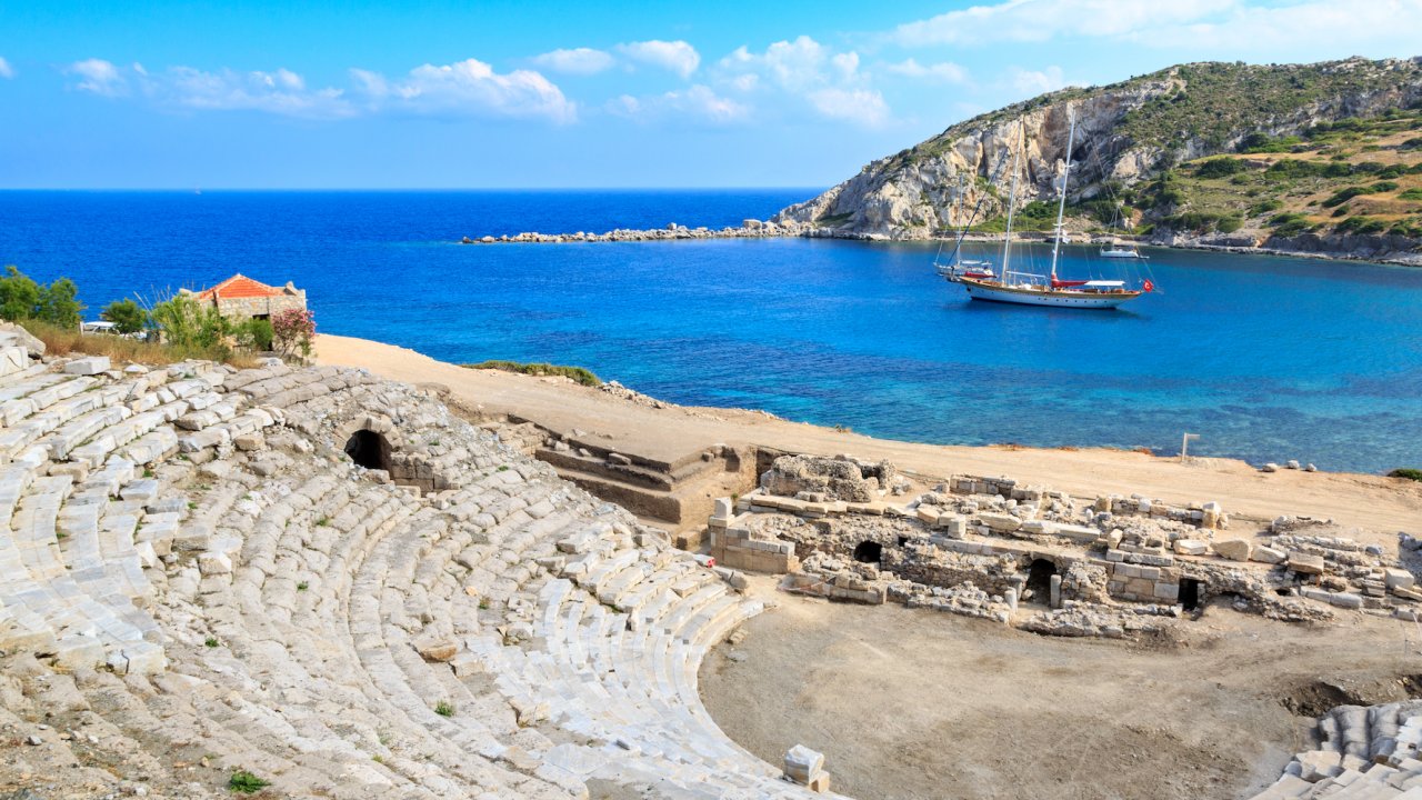 A sail boat with rooms aboard cruising past a historic amphitheater in Turkey