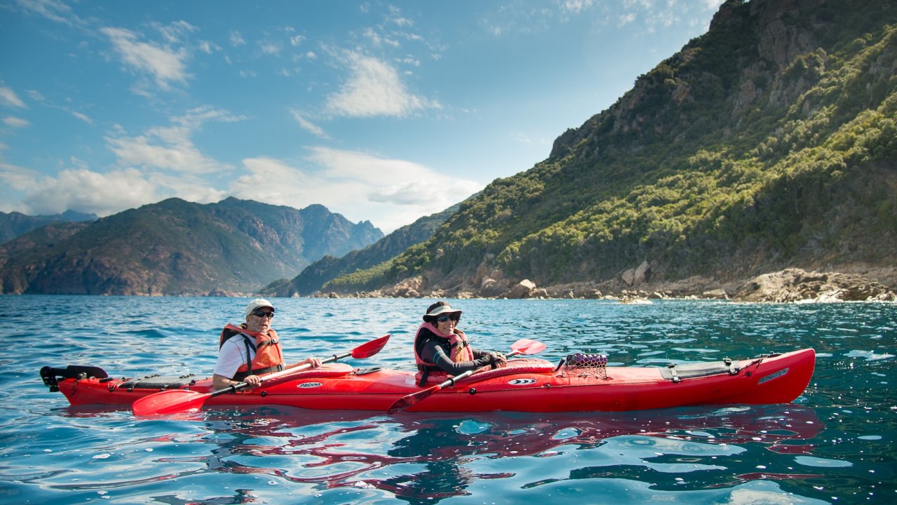 A couple sea kayaking on calm waters outside of Corsica.