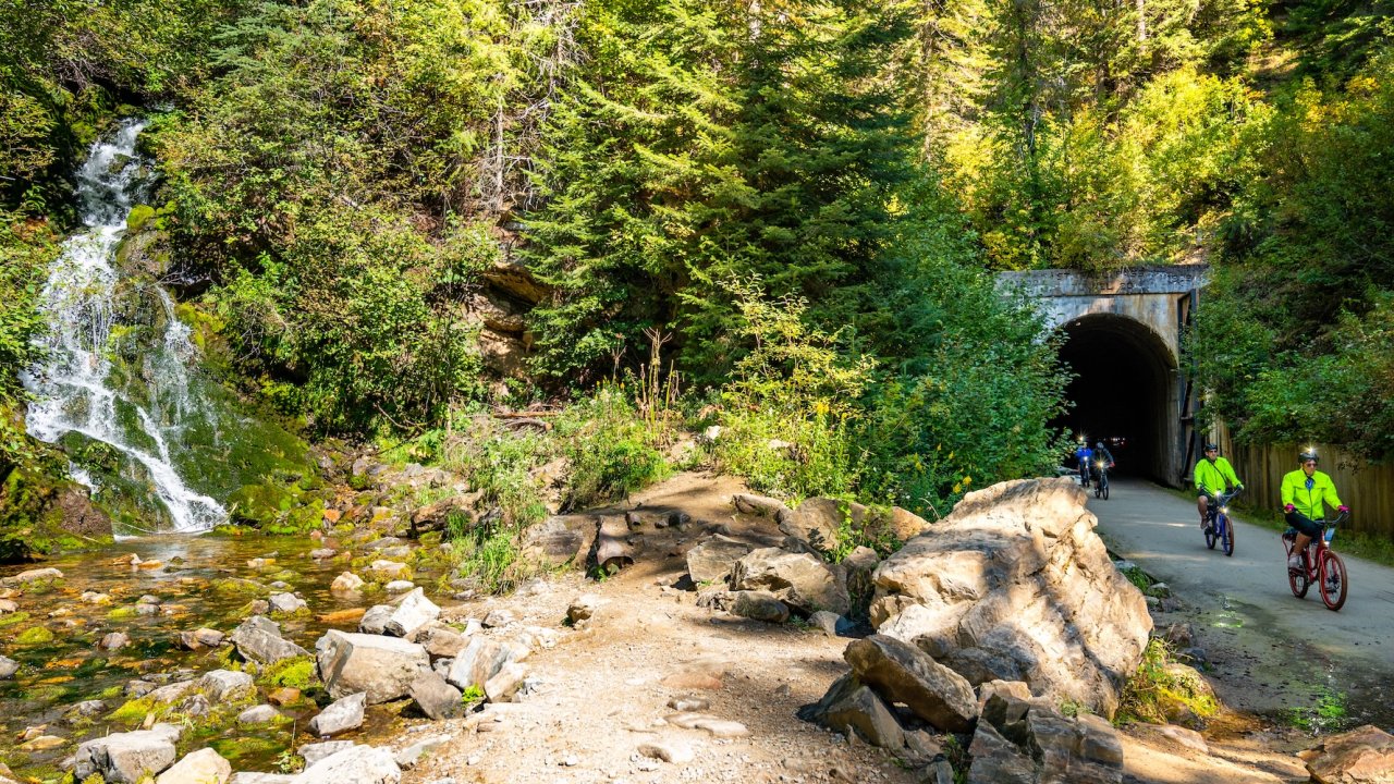 Cyclists exiting a tunnel beside a waterfall on the Route of the Hiawatha biking trail
