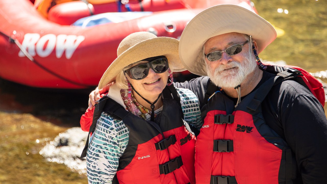 A couple sitting on a red whitewater raft smiling