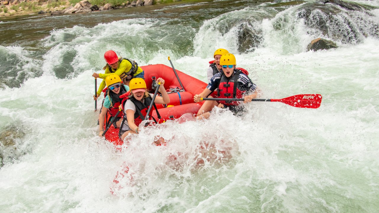 A group of people in a red raft paddling through a whitewater rapid in Idaho