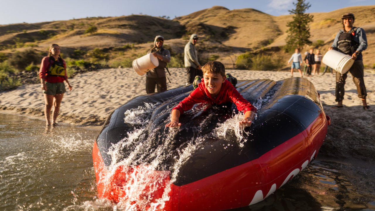 A kid sliding down a red whitewater raft that was turned upside down