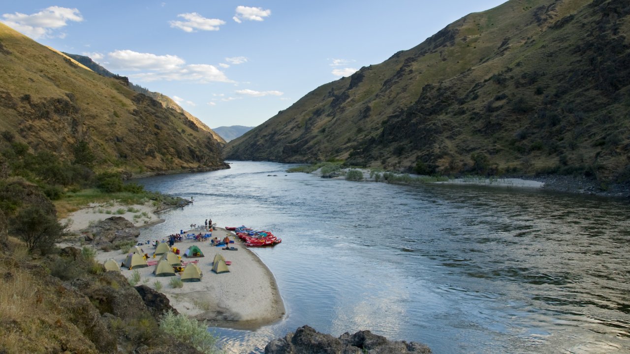 Ten tents on a sandy beach along the Salmon River at sunset