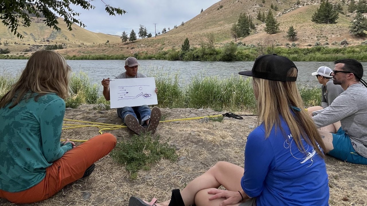 ROW Adventures guide Tom Scarbrough teaching a circle of people how to navigate a raft through a rapid along the Deschutes River