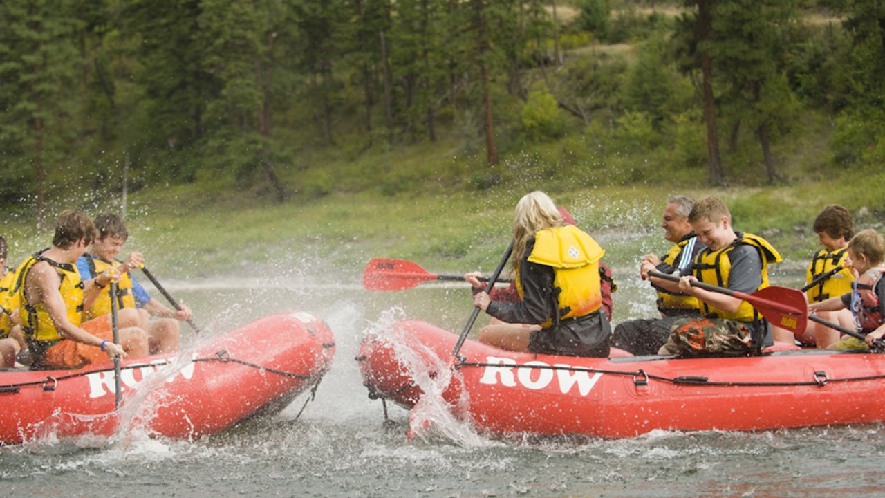 Guests on two whitewater rafts splashing each other with their paddles.