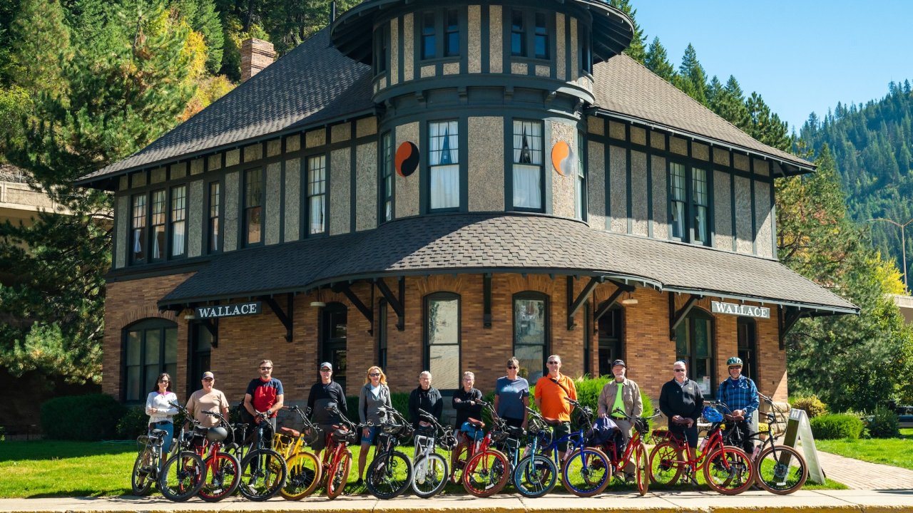 Group of cyclists posing with colorful bikes in front of the historic Wallace train station in Idaho