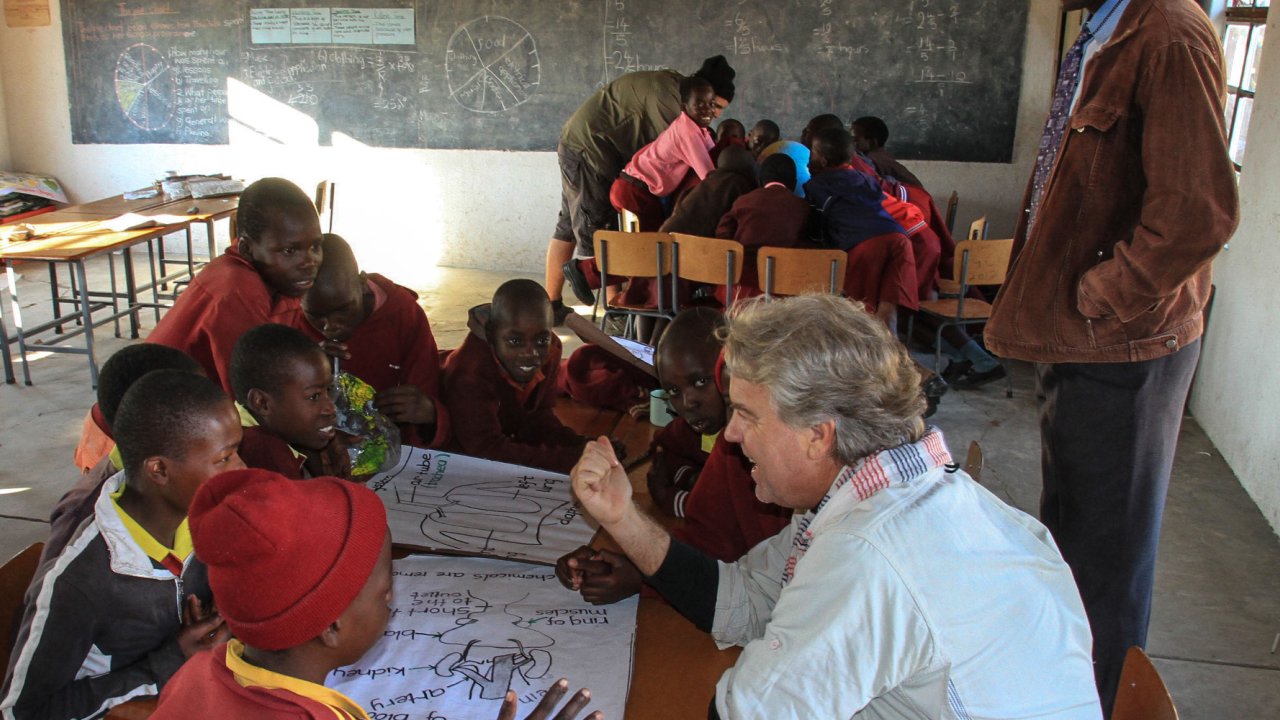 A tourist sitting around a table with kids from Africa in their classroom