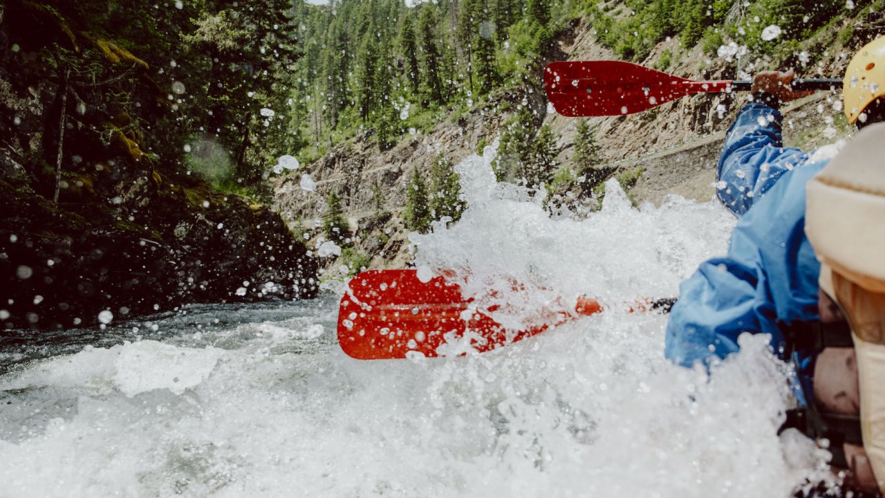 River left shot of red paddles moving through a big splashy wave with paddlers on the right side of the photo