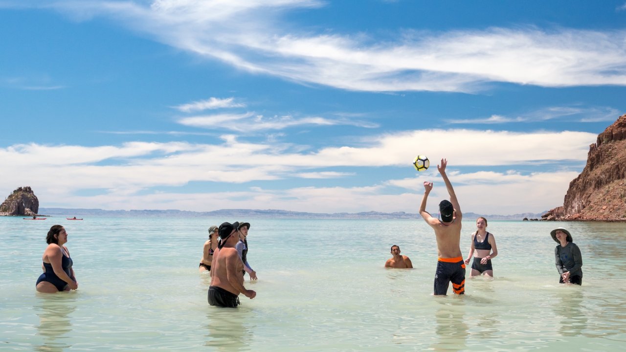 Beach vacation for families with parents and kids playing volleyball in shallow ocean water on a sunny family getaway