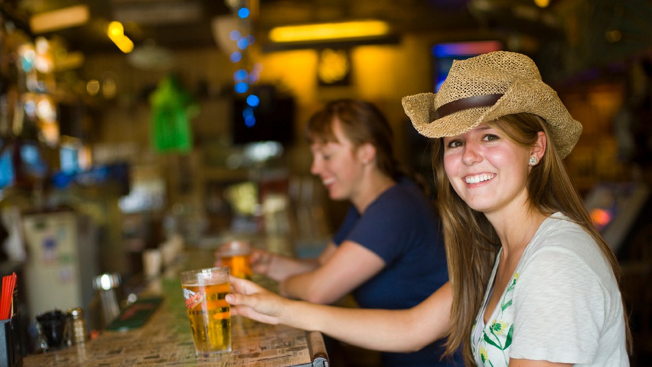 A smiling woman sitting at the bar in a brewery enjoying a beer while on a guided biking tour.