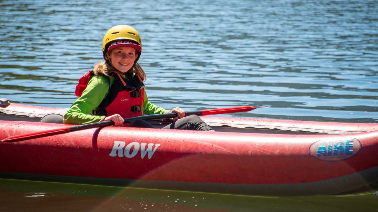 Young rafter paddling an inflatable kayak on Idaho’s Clearwater River during a sunny summer day, wearing a yellow helmet and red life jacket with ROW Adventures logo visible — perfect family-friendly rafting trip in Idaho.