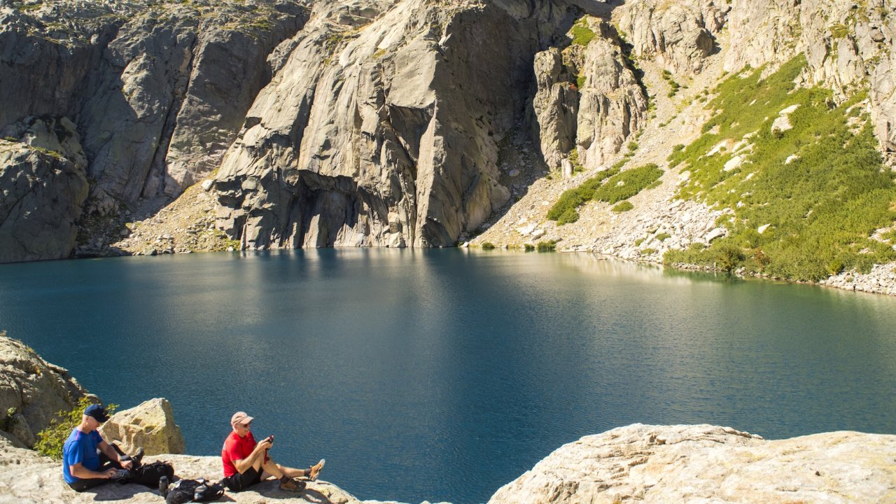 Hikers relax beside a high alpine lake in Corsica’s mountains, a highlight of the island’s hiking routes on a guided Corsica tour.
