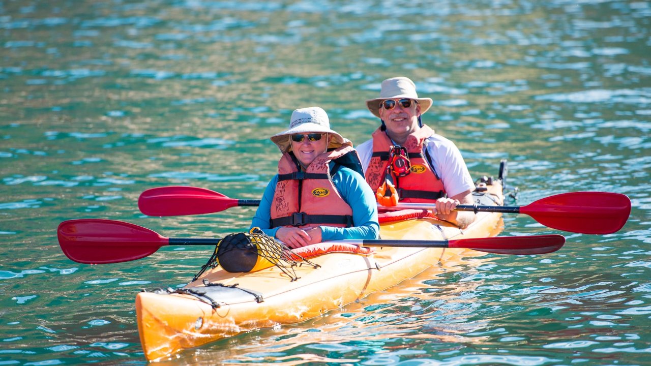 Travelers paddle a tandem sea kayak on calm coastal waters in Corsica as part of a small-group Corsica tour.