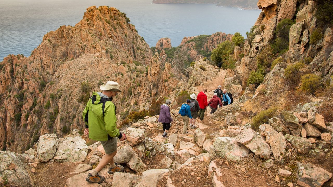 A small group hikes along a dramatic coastal trail in Corsica, combining mountain terrain and sea views on an active Corsica travel itinerary.