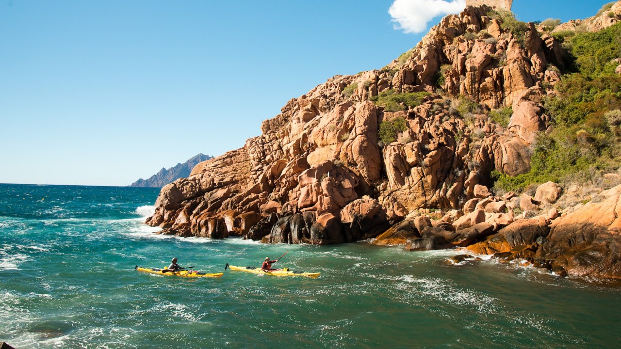 Sea kayakers explore Corsica’s dramatic rocky shoreline, experiencing the island from the water on an active Corsica travel itinerary.