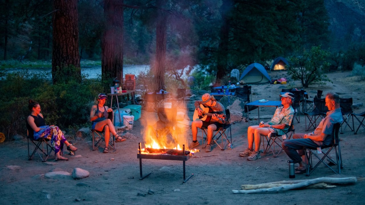 Guests relaxing around a glowing campfire on the banks of the Middle Fork of the Salmon River, enjoying music and wilderness camping in Idaho’s backcountry.